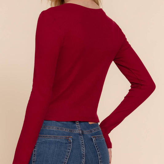Woman wearing a red long-sleeve top and blue jeans on a beige background