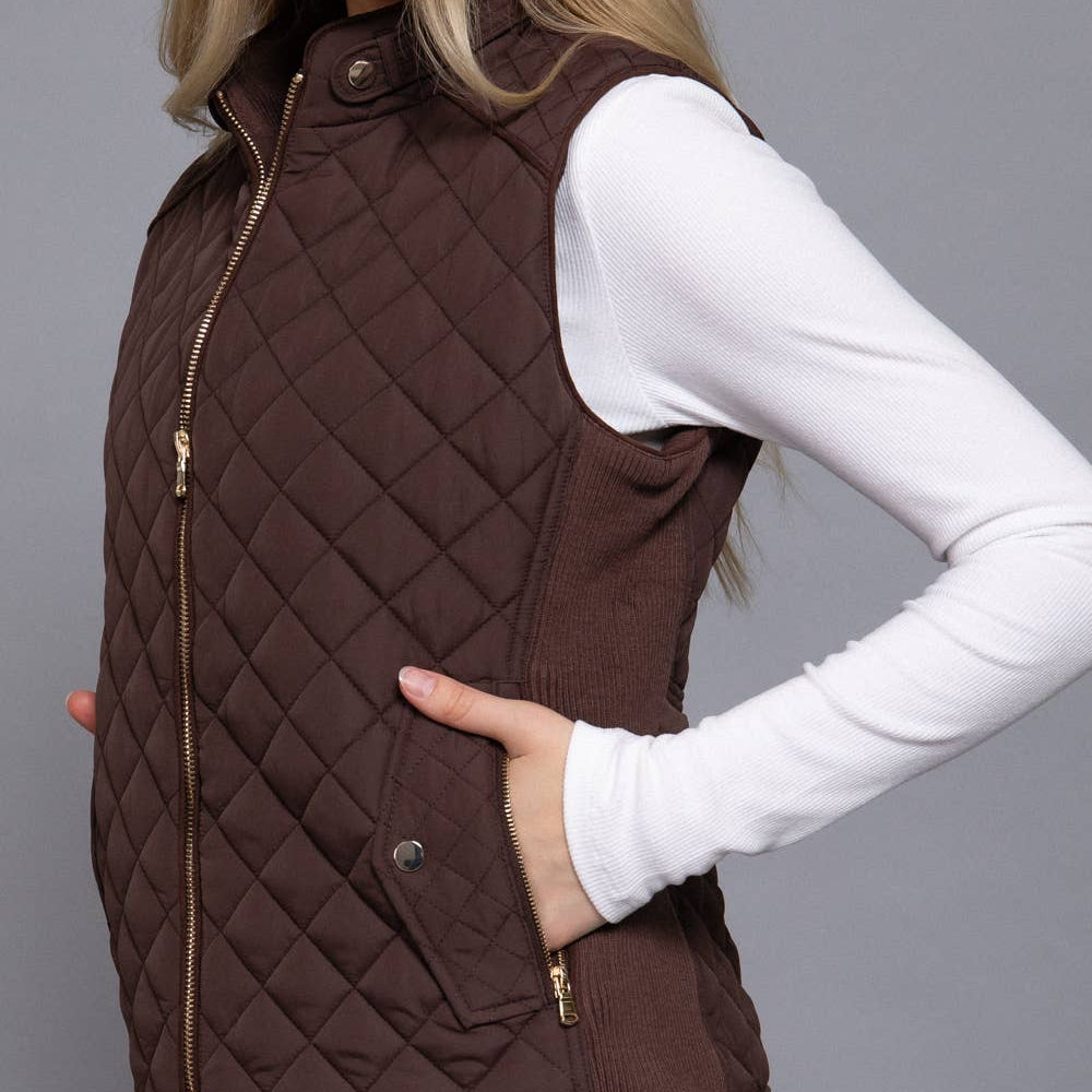 Woman wearing a brown quilted vest over a white long-sleeve shirt on a gray background