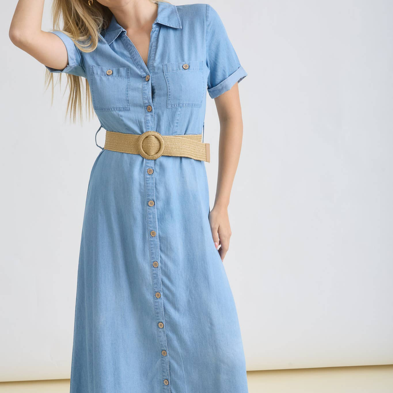 Woman wearing a light blue dress with a beige belt against a white background