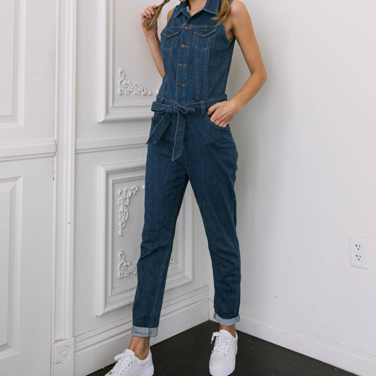 Woman wearing a denim jumpsuit standing against a white wall.