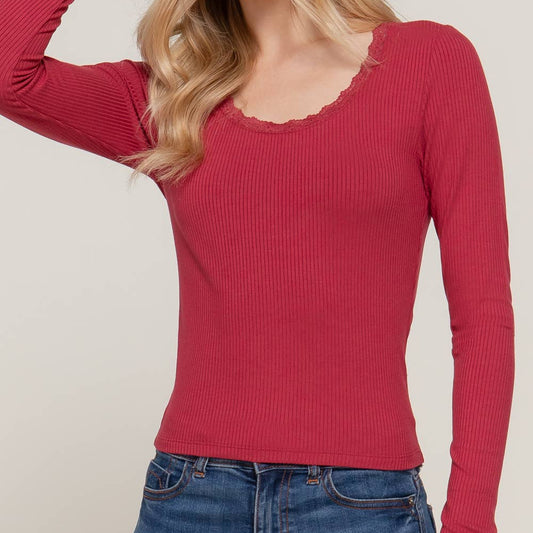Woman wearing a red ribbed long-sleeve top and blue jeans against a plain background