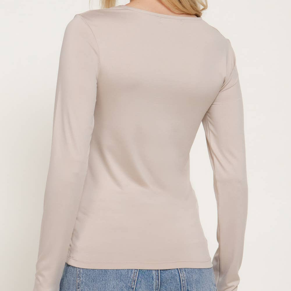 A woman shown from the back wearing a fitted, long-sleeve beige top and blue jeans against a plain light background.