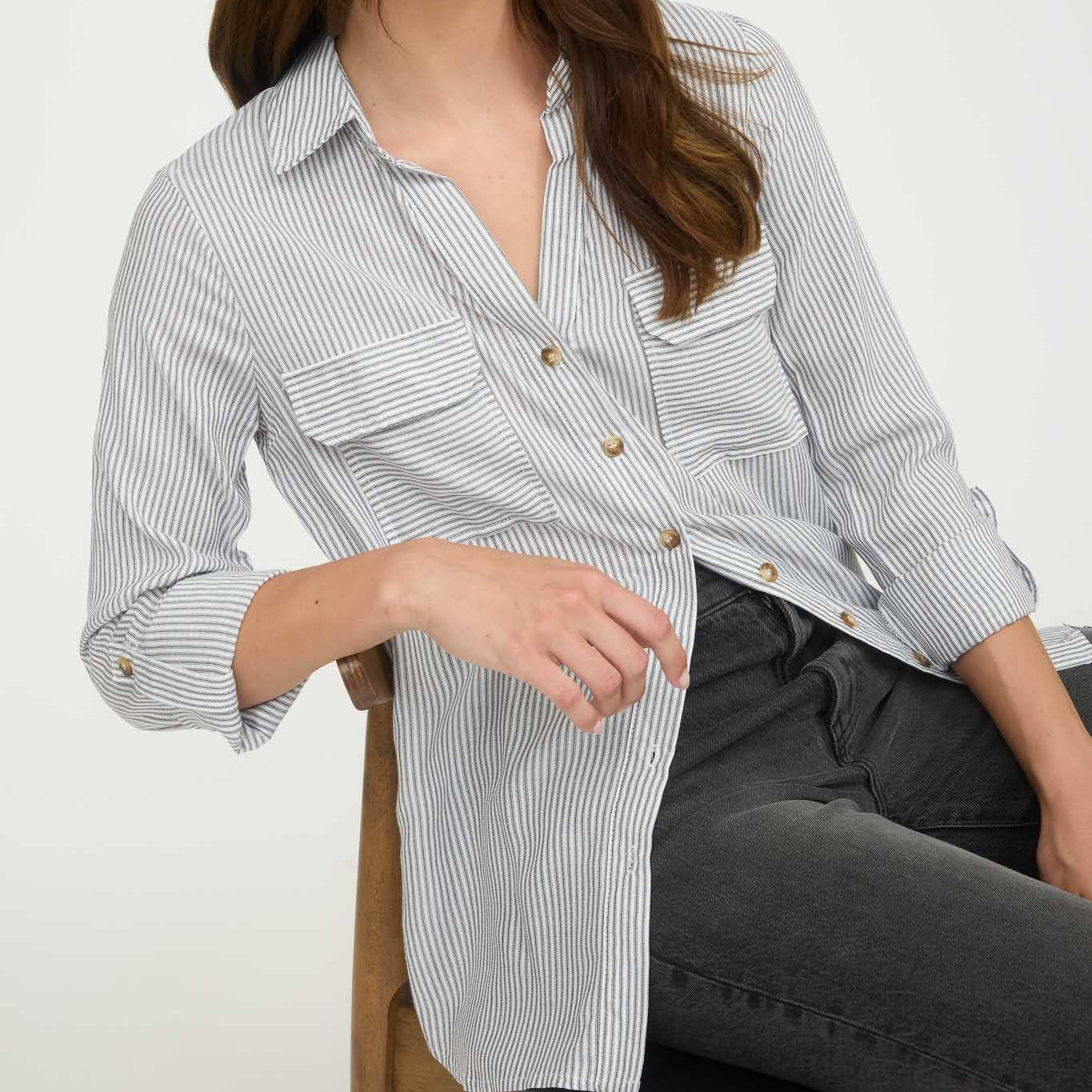 Woman wearing a striped shirt sitting on a chair against a white background