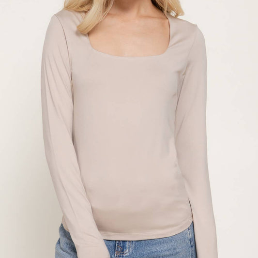 A woman modeling a beige long-sleeve scoop-neck top paired with blue jeans against a plain light background.