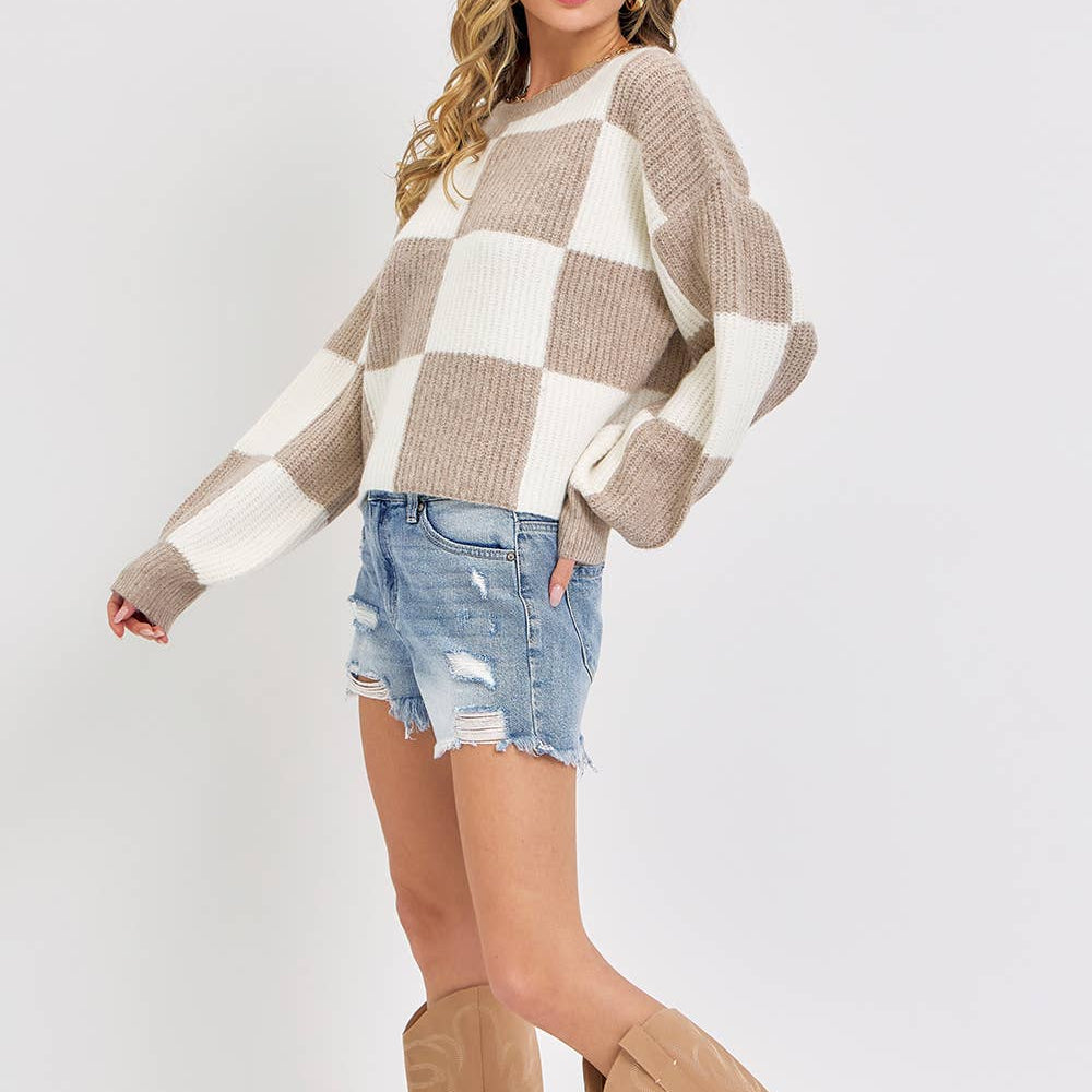 Woman wearing a checkered sweater, denim shorts, and tan knee-high boots on a white background