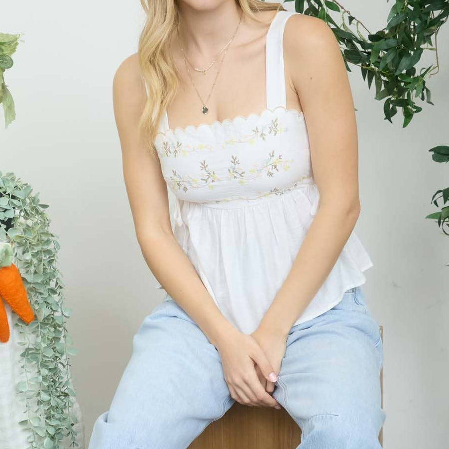 Woman sitting on a wooden stool wearing a white top and light blue jeans, with a decorated table in the background.