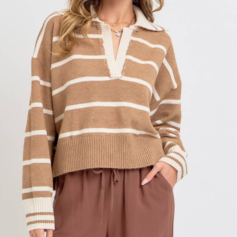 A woman modeling a cropped knit sweater with horizontal beige and off-white stripes, featuring a mock neck with a frayed trim and ribbed cuffs and hem, paired with brown drawstring pants against a light gray studio background.