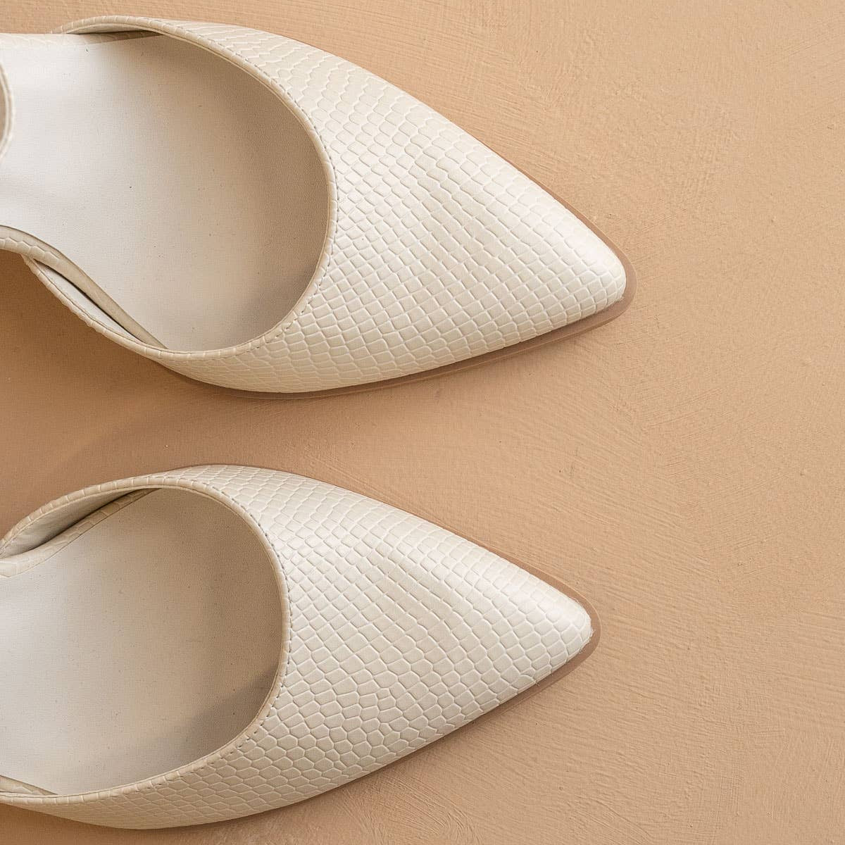 Pair of white pointed-toe shoes on a beige background