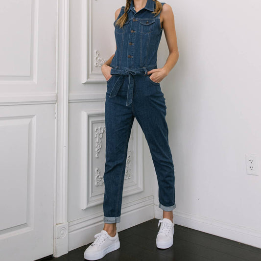 Woman wearing a denim jumpsuit standing in a room with white walls and a door.