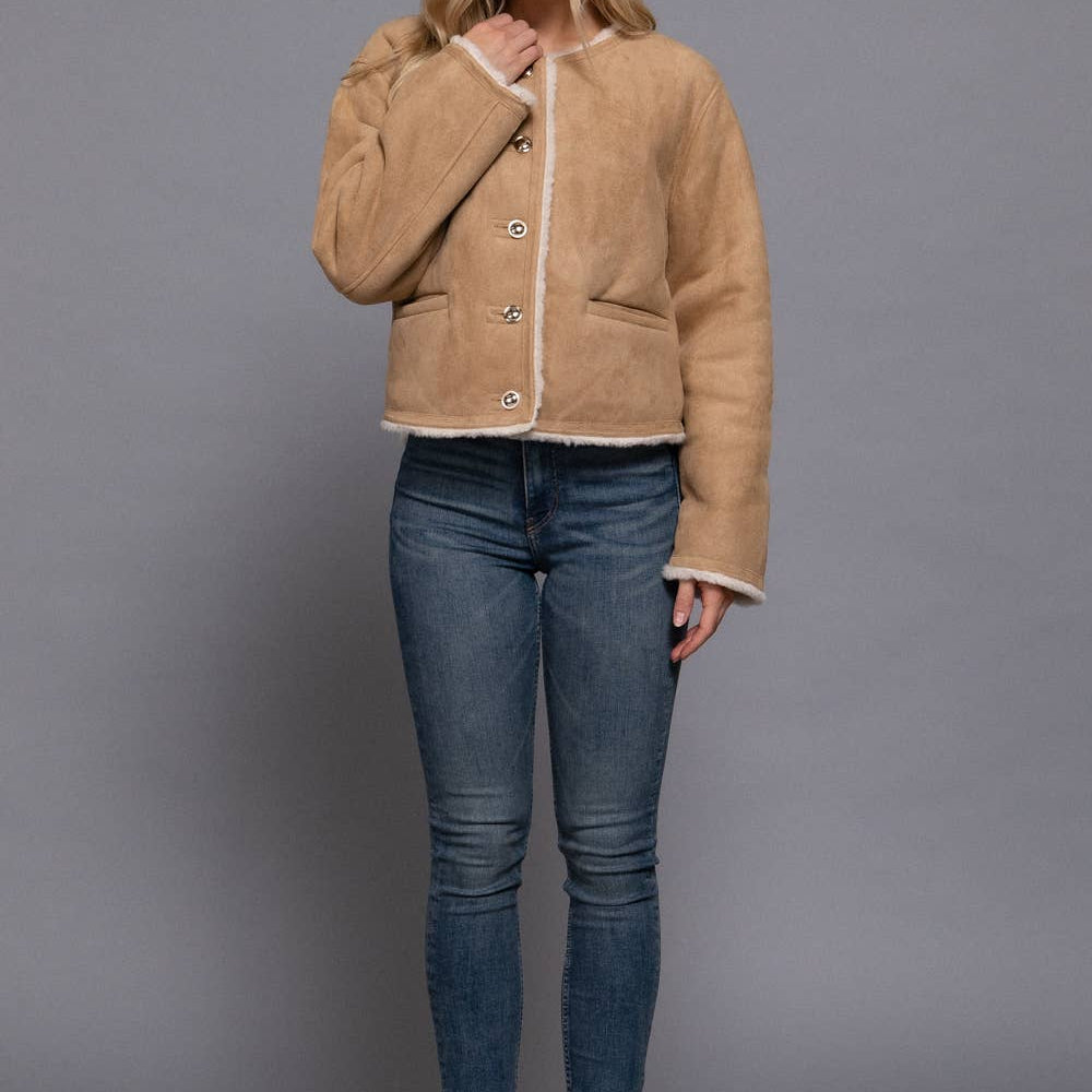 Woman wearing a beige jacket, blue jeans, and black boots on a gray background