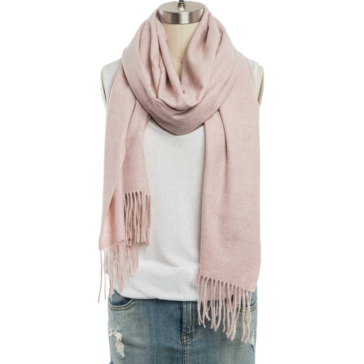 A dusty pink knit scarf with fringe ends, draped around a mannequin torso wearing a white sleeveless top and blue jeans against a plain white background.