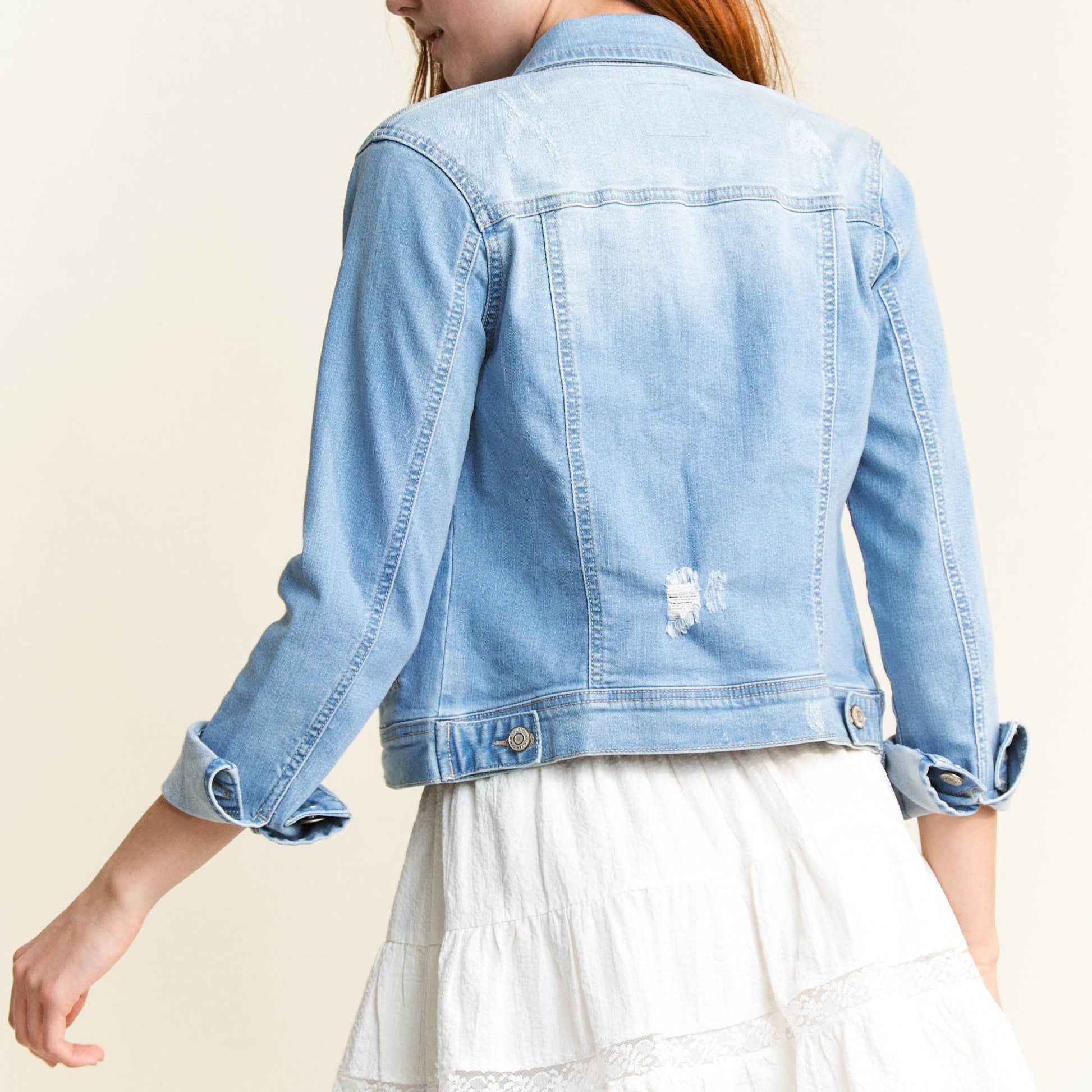 Woman wearing a light blue denim jacket and white dress on a beige background