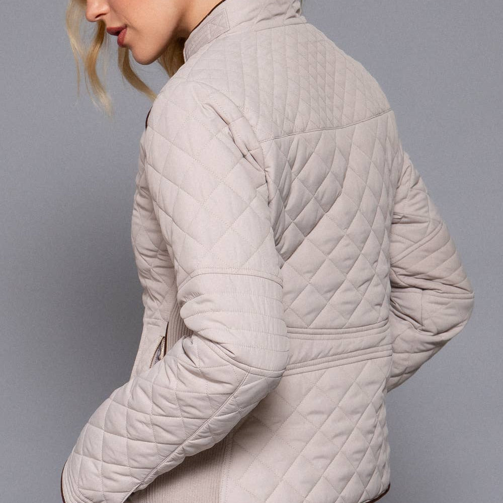 Woman wearing a beige quilted jacket against a gray background