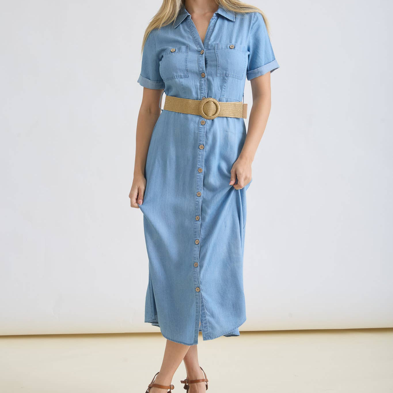 Woman wearing a light blue denim dress with a belt on a white background