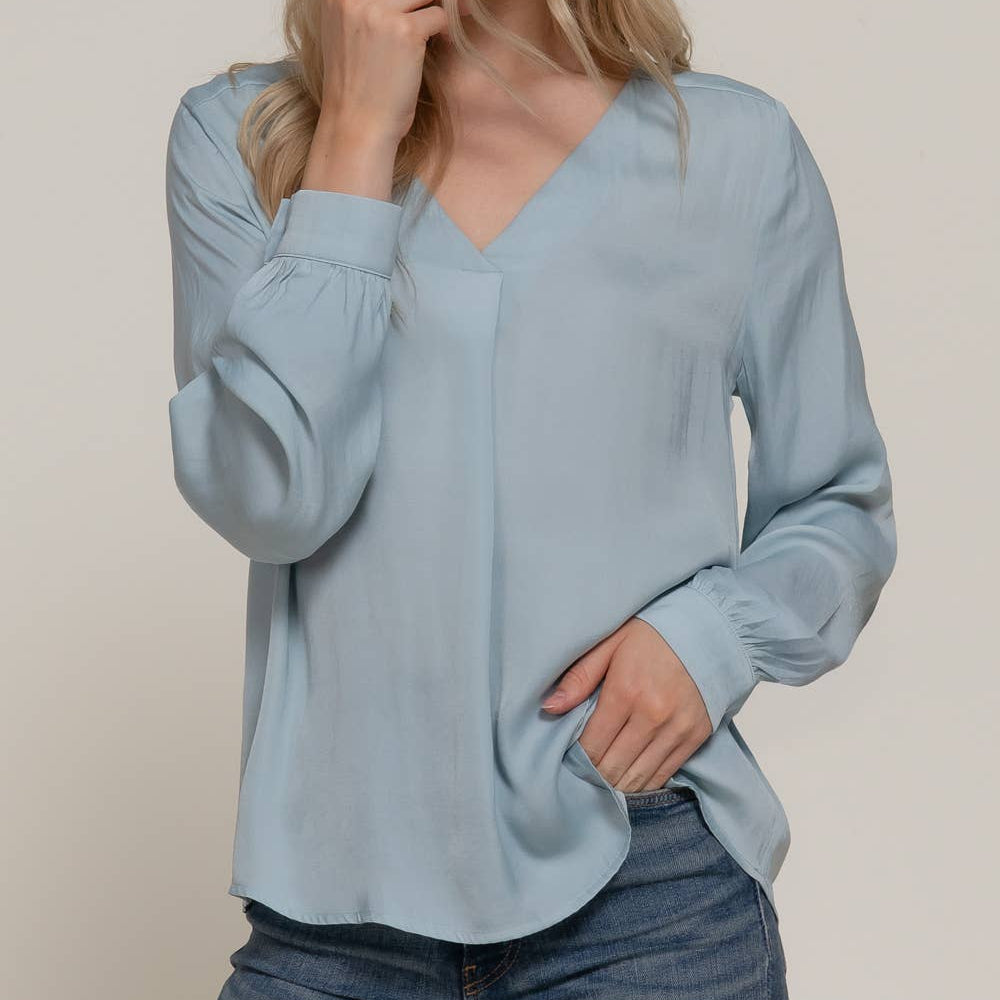 Woman wearing a light blue blouse and jeans against a plain background