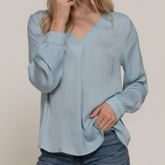 Woman wearing a light blue blouse and jeans against a plain background