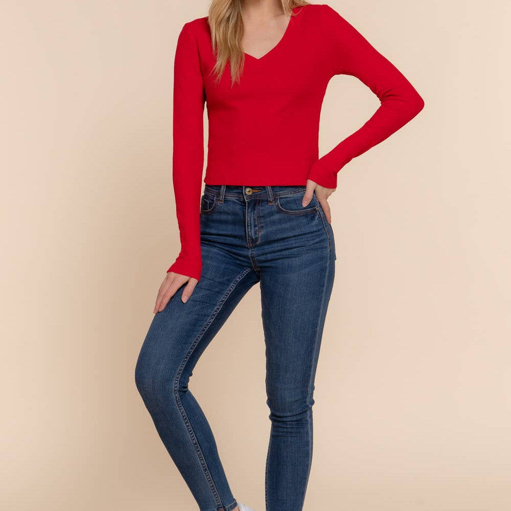 Woman wearing a red long-sleeve top and blue jeans on a beige background