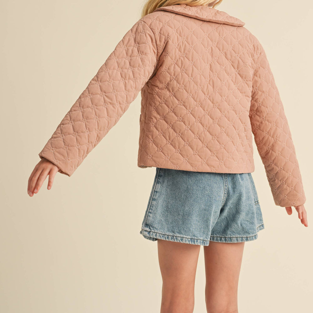 Person wearing a pink quilted jacket and denim shorts on a beige background