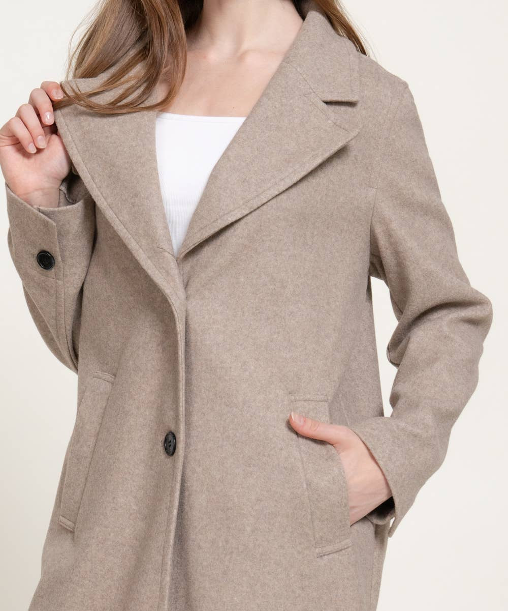 A woman wearing a light taupe-beige wool-blend coat over a white top, shown from the nose down against a plain light background.