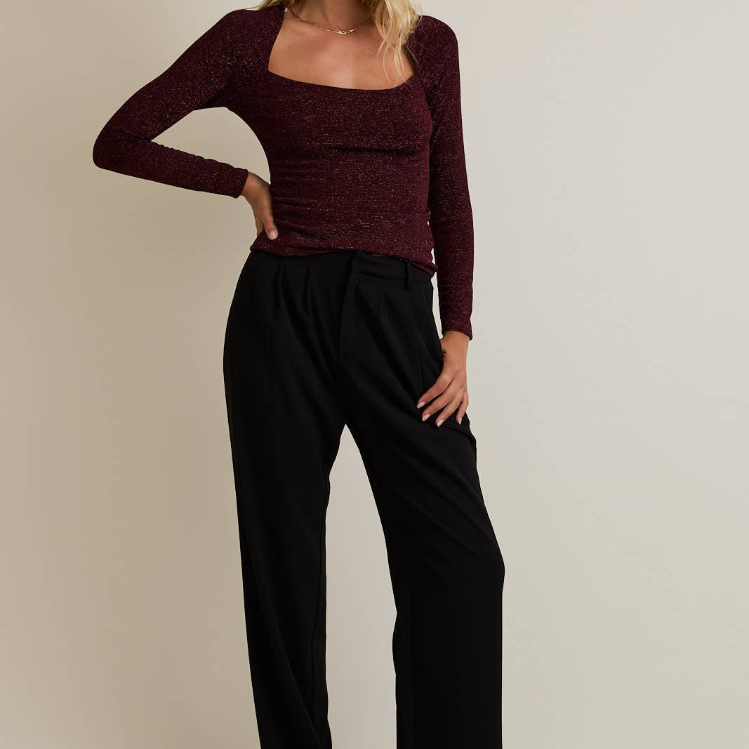 Woman wearing a burgundy top and black pants against a beige background