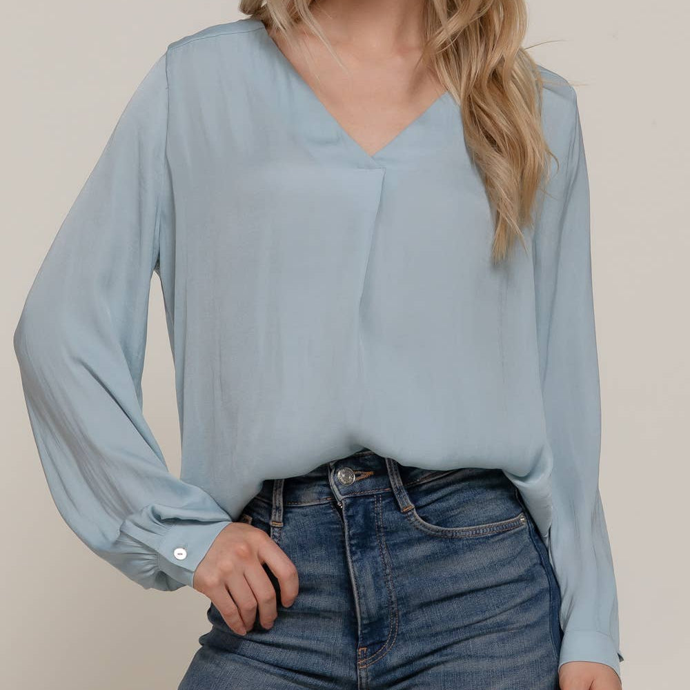 Woman wearing a light blue blouse and jeans against a beige background