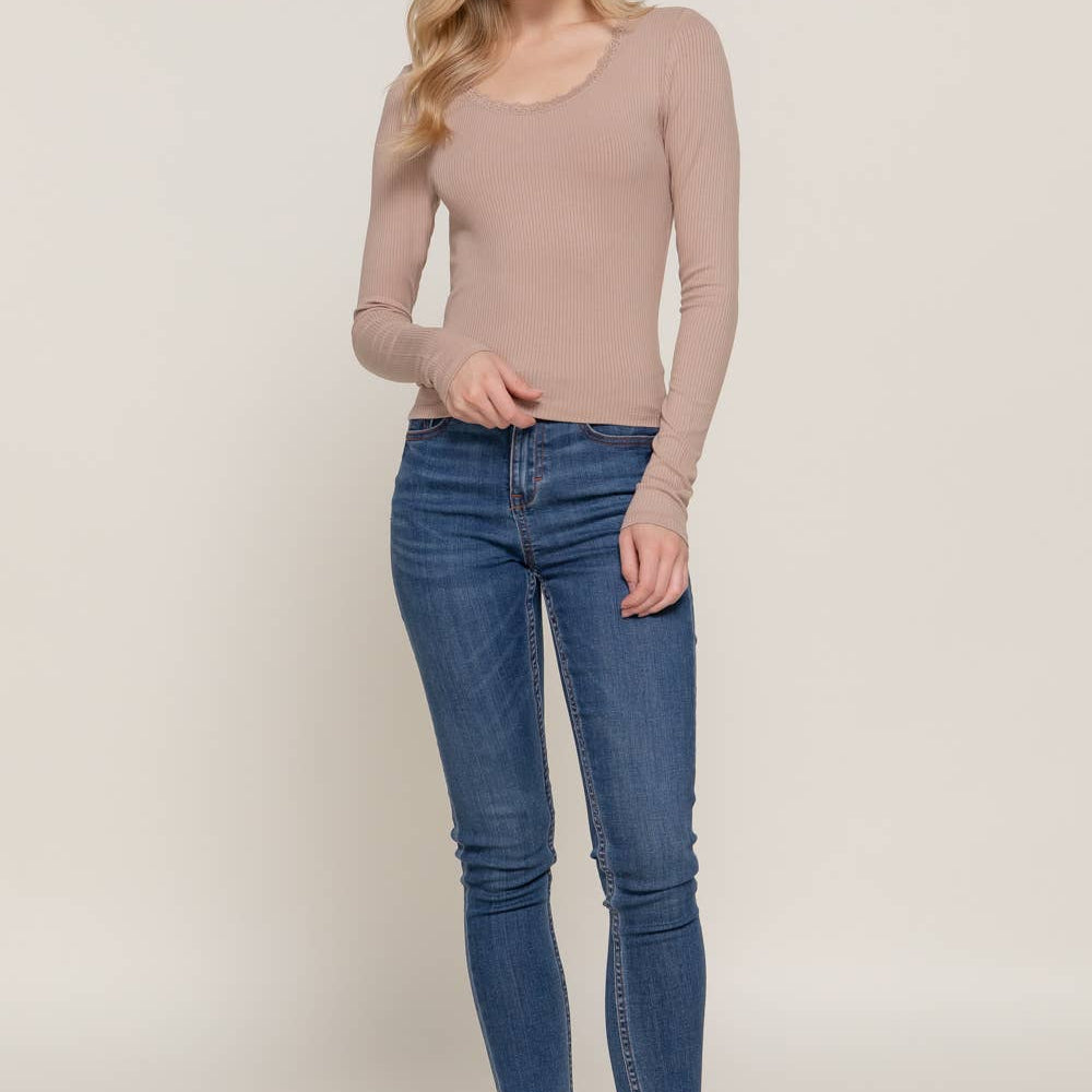 Woman wearing a beige long-sleeve top and blue jeans on a plain background