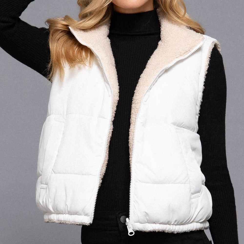 Woman wearing a white puffer vest over a black outfit against a gray background