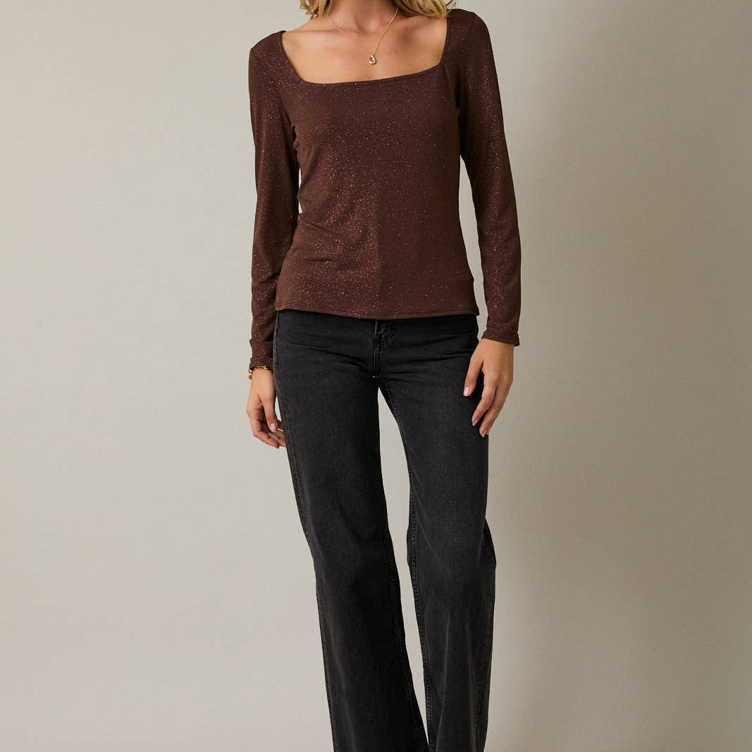 Woman wearing a brown long-sleeve top and black pants against a neutral background