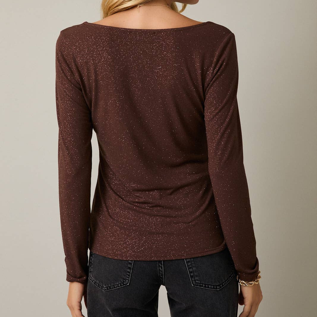 Woman wearing a brown long-sleeve top and dark jeans against a neutral background