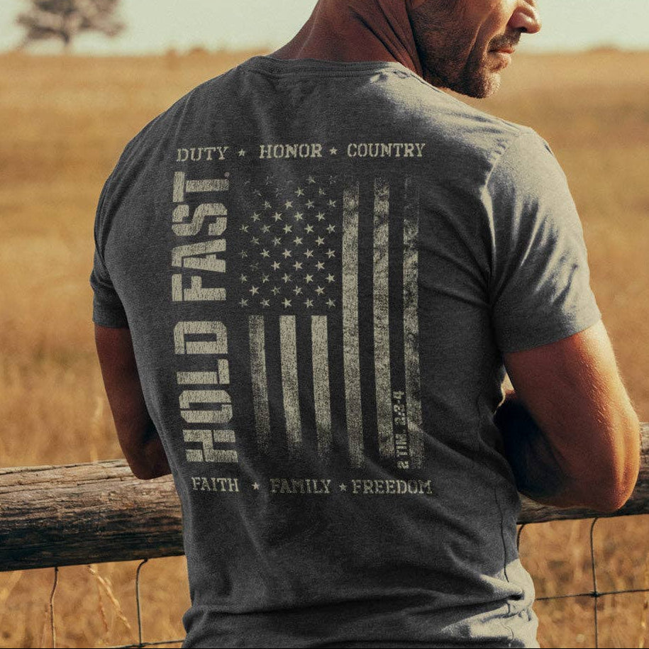 Man wearing a t-shirt with an American flag design and text, standing in a field.