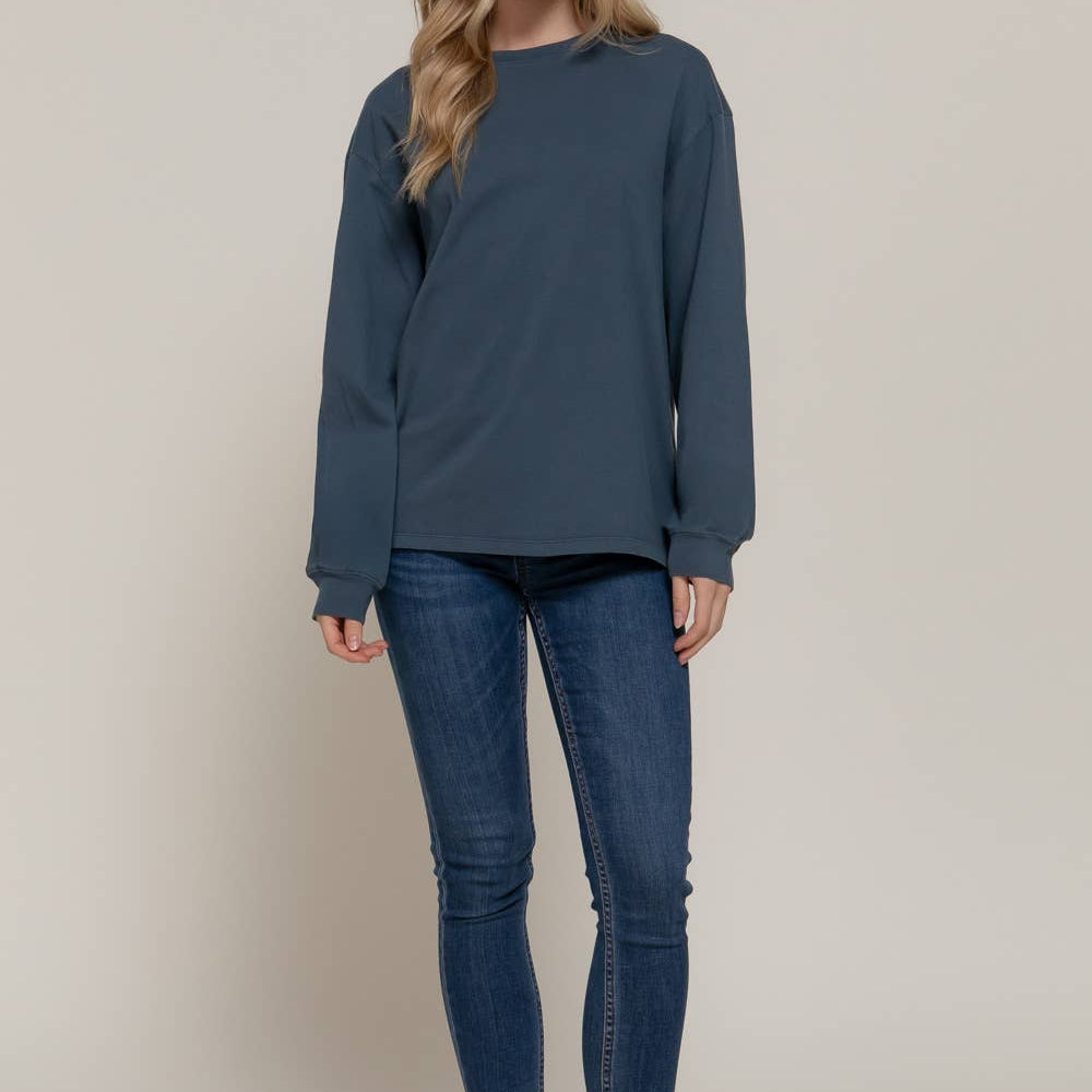 Woman wearing a blue long-sleeve top and jeans on a plain background