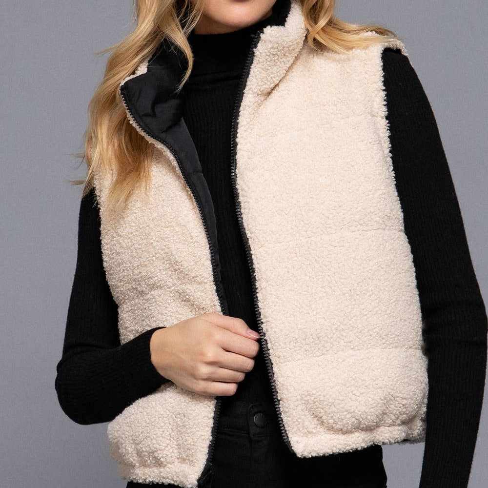 Woman wearing a beige fleece vest over a black outfit on a gray background