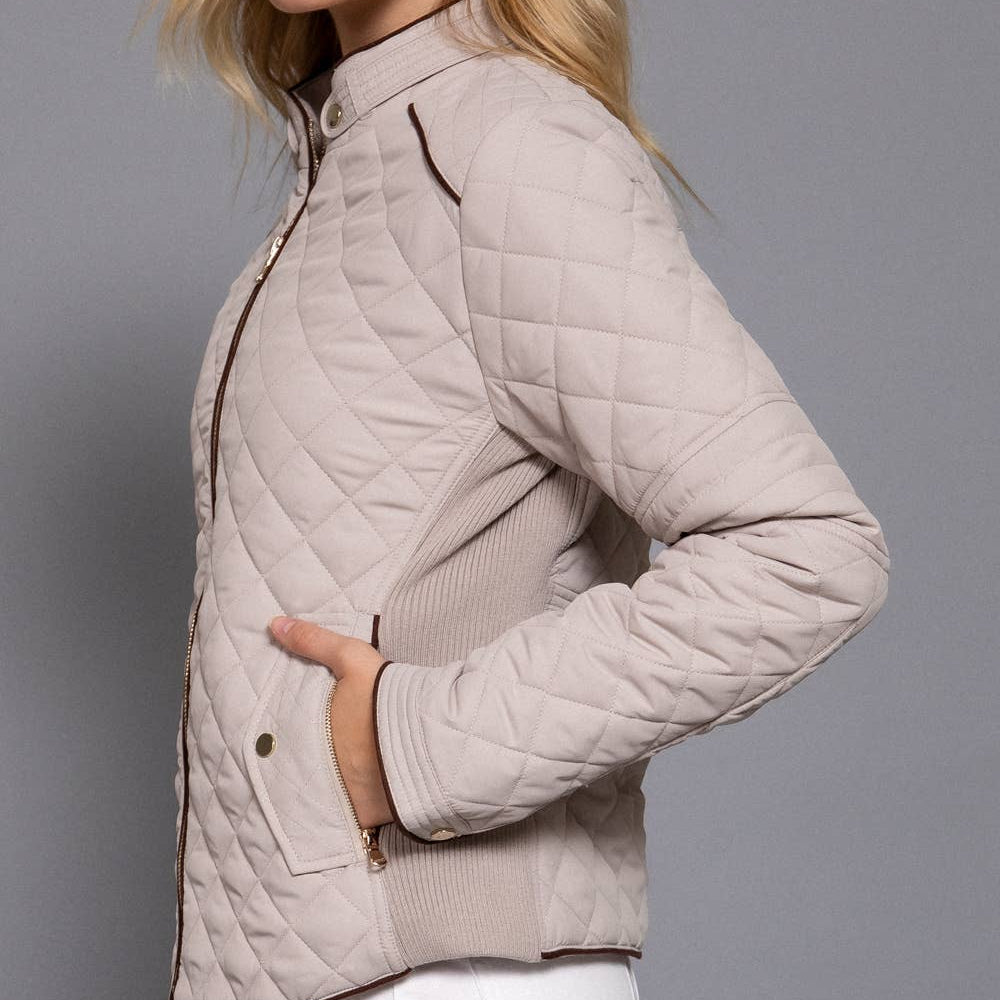 Woman wearing a beige quilted jacket against a gray background