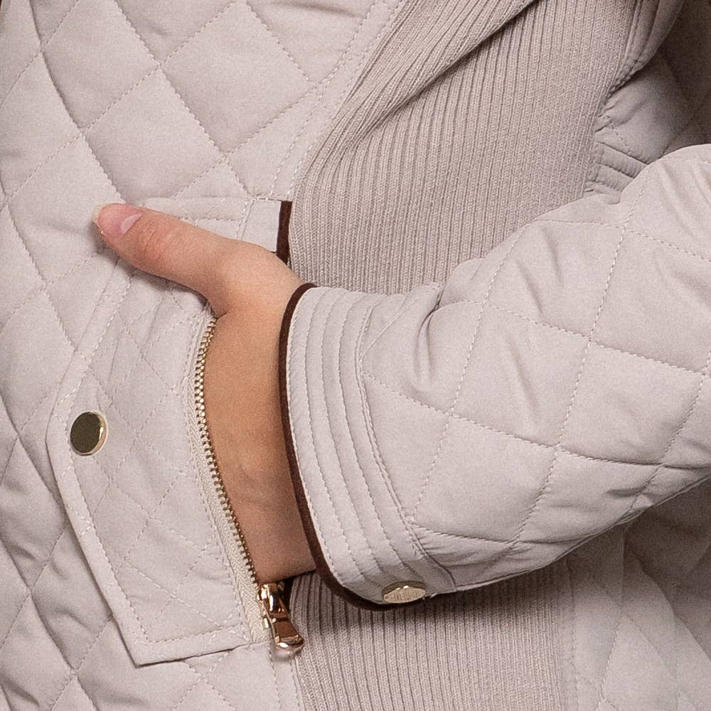 Close-up of a person wearing a light gray quilted jacket with a hand on the chest area.