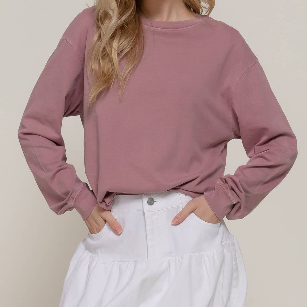 Woman wearing a mauve long-sleeve top and white skirt against a beige background