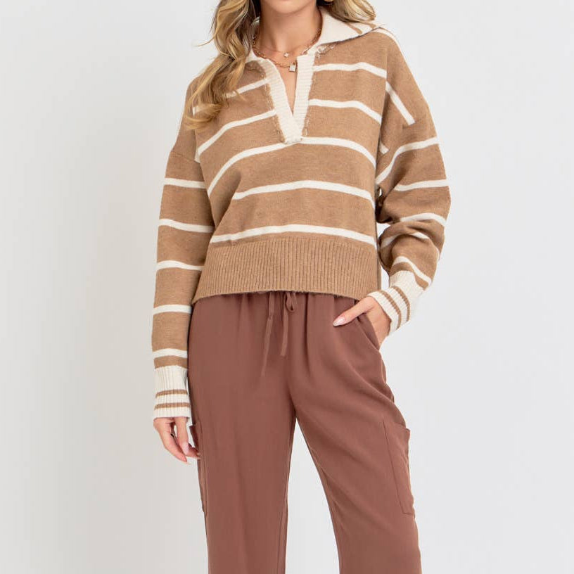 A woman modeling a brown and beige horizontally striped knit sweater with a half-placket and white collar, paired with brown wide-leg drawstring pants and tan sandals, against a light gray studio background.