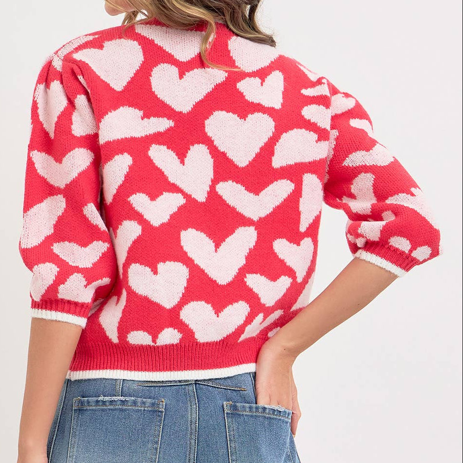 Person wearing a red sweater with white heart patterns on a plain background