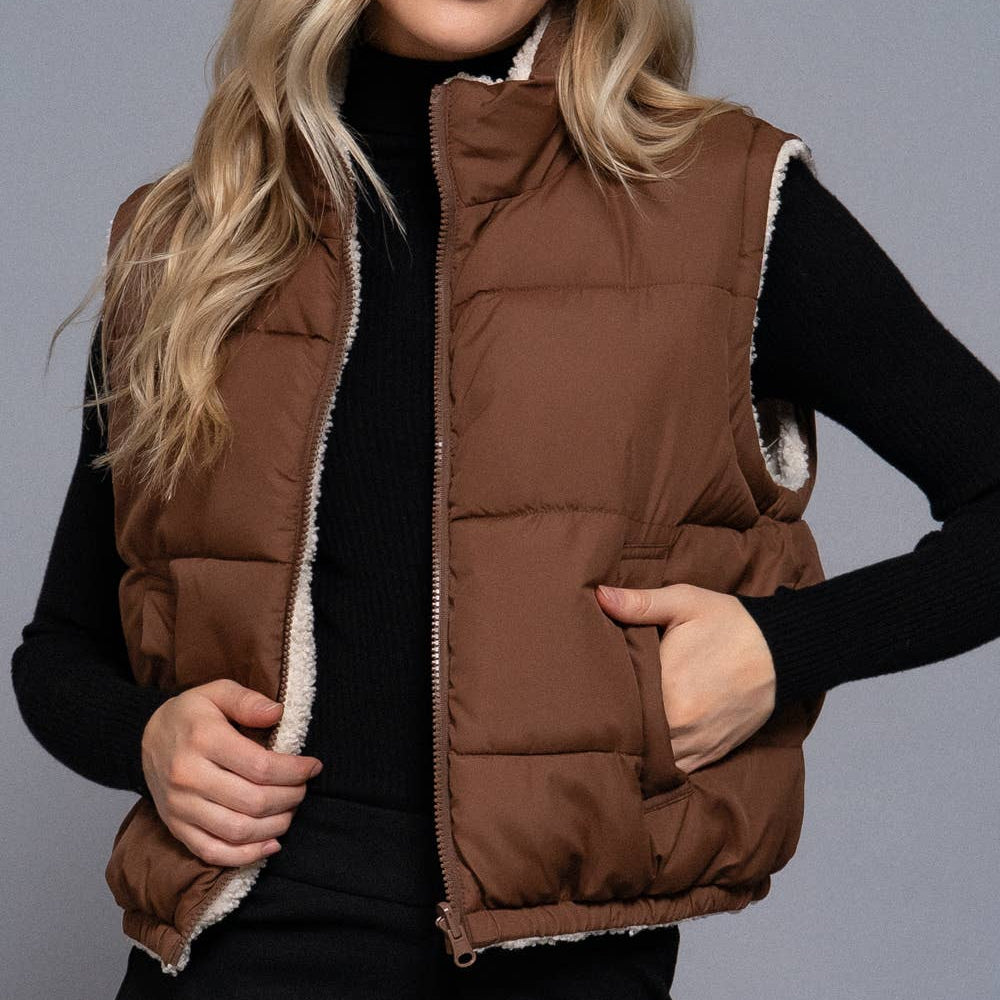 Woman wearing a brown puffer vest over a black outfit on a gray background