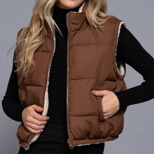 Woman wearing a brown puffer vest over a black outfit on a gray background