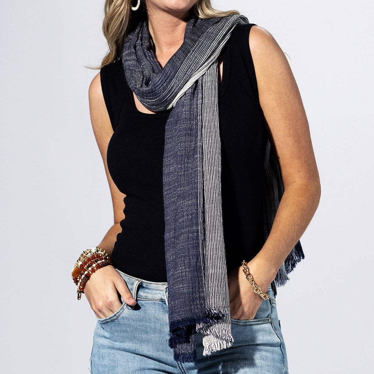 Woman wearing a black sleeveless top, blue jeans, and a gray scarf on a white background