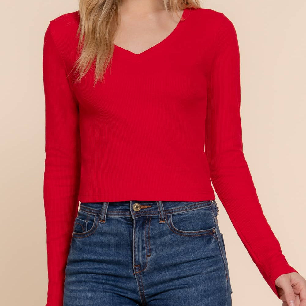 Woman wearing a red long-sleeve top and blue jeans on a beige background