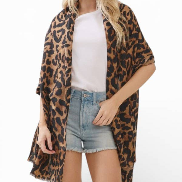 A blonde woman modeling a leopard print open-front shawl or kimono over a white t-shirt and denim shorts, set against a plain white studio background.