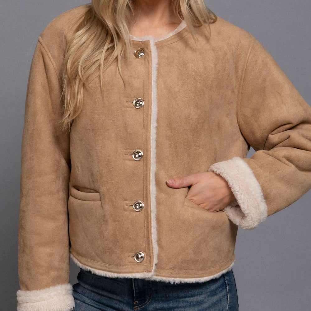 Woman wearing a tan shearling jacket with white trim on a gray background