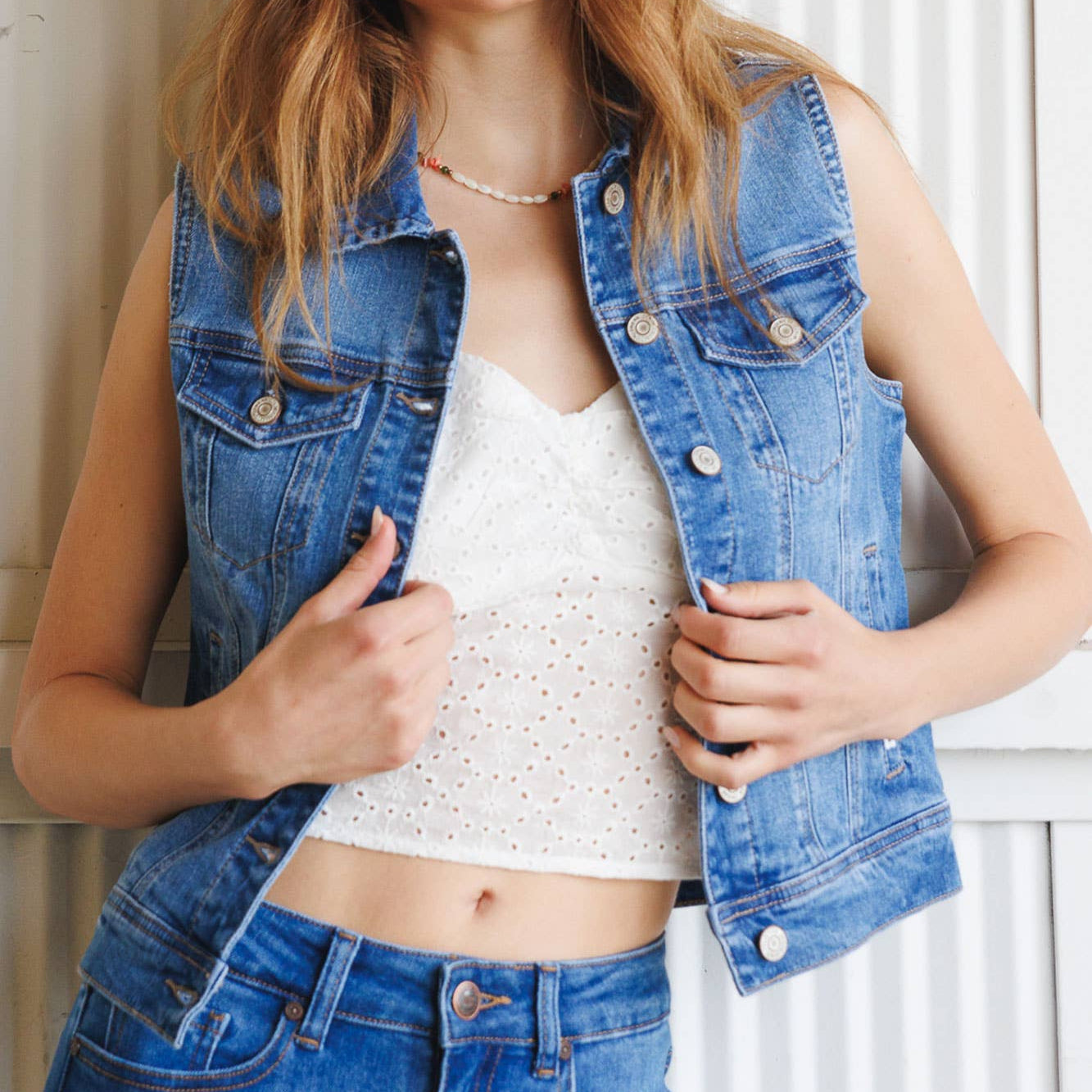 Woman wearing a denim vest over a white top against a white background