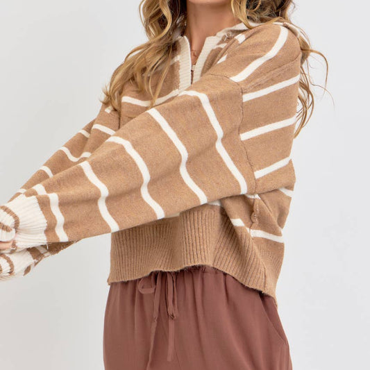 A woman wearing a cropped knit sweater with beige and white horizontal stripes, paired with brown drawstring pants, photographed against a light gray studio background.