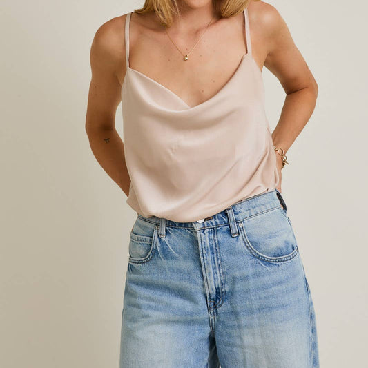 Woman wearing a beige tank top and blue jeans against a plain background