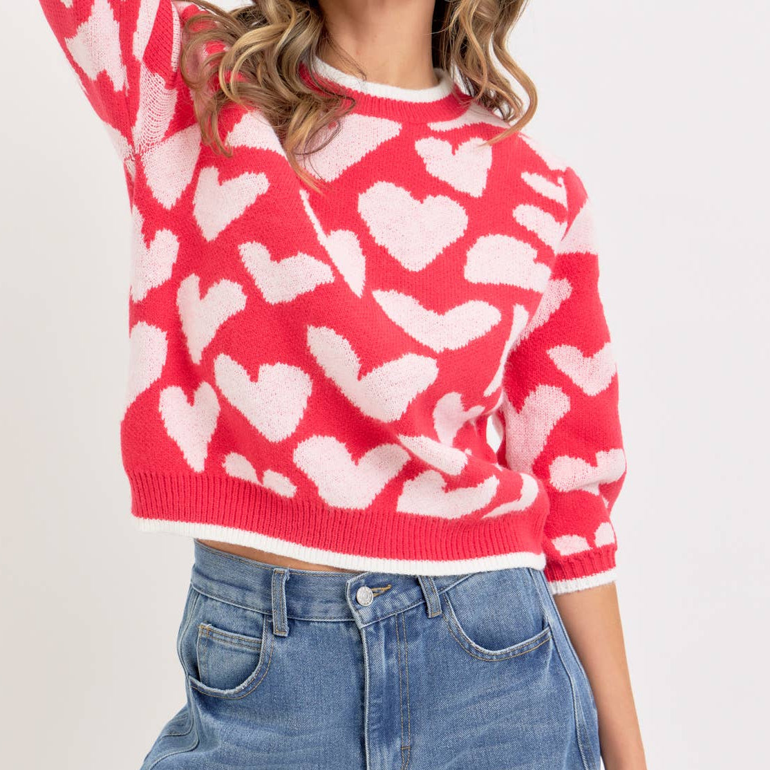 Woman wearing a red sweater with white heart patterns and blue jeans on a white background