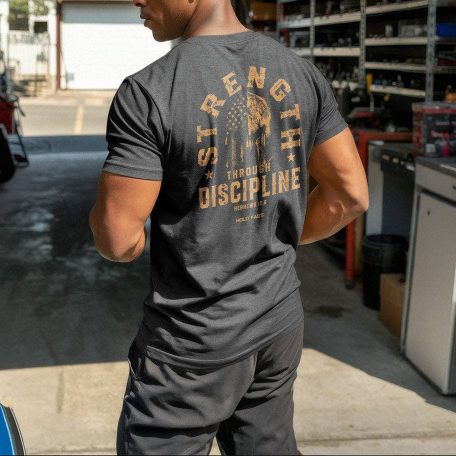 Man wearing a 'Strength Through Discipline' t-shirt in a garage.