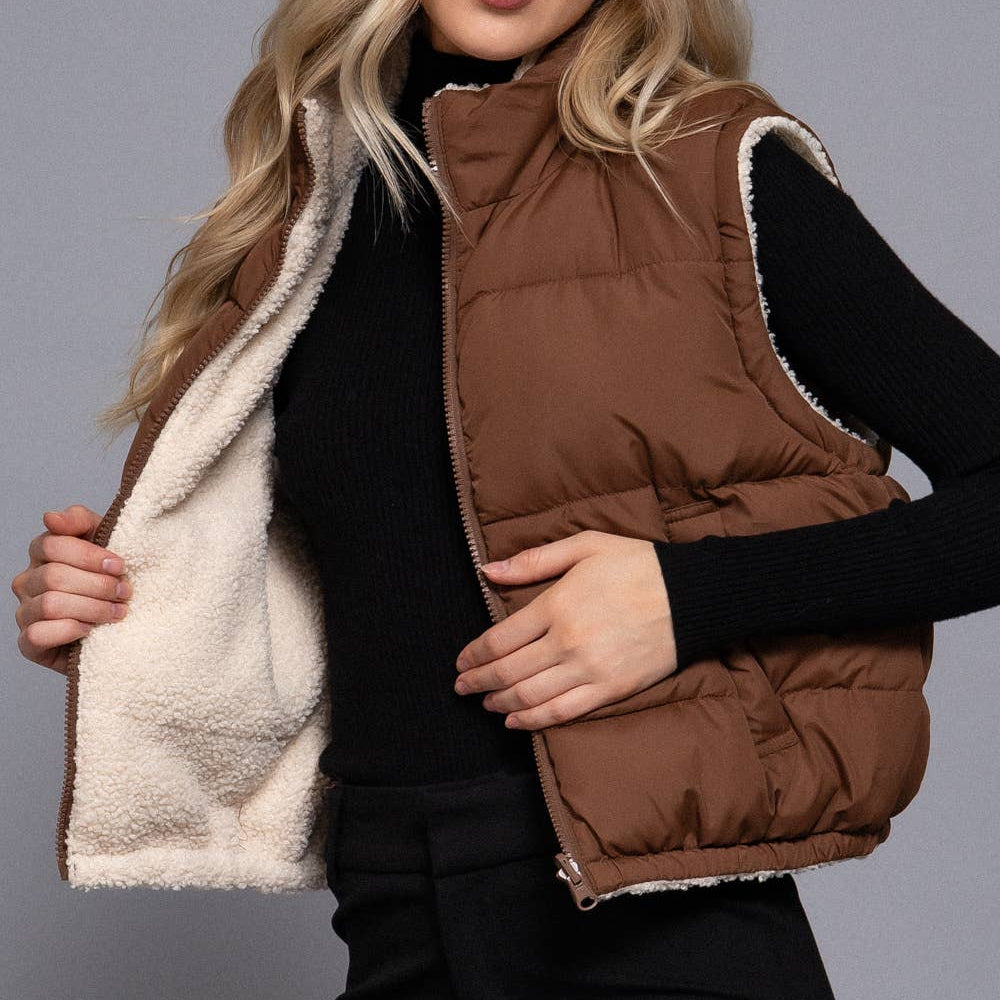 Woman wearing a brown puffer vest with white interior on a gray background