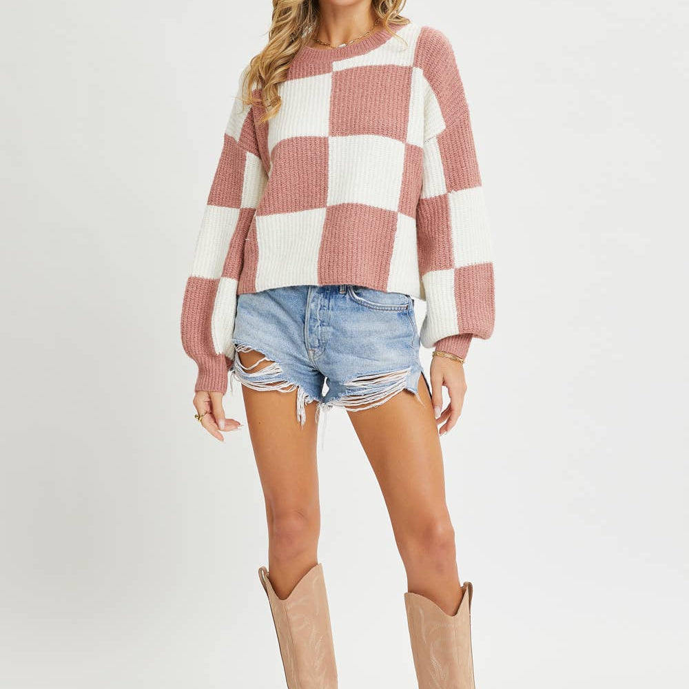 Woman wearing a checkered sweater, denim shorts, and tan boots on a white background